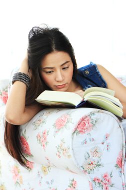 yorgun genç kadın evde kanepenin üzerine bir kitap okuma. 