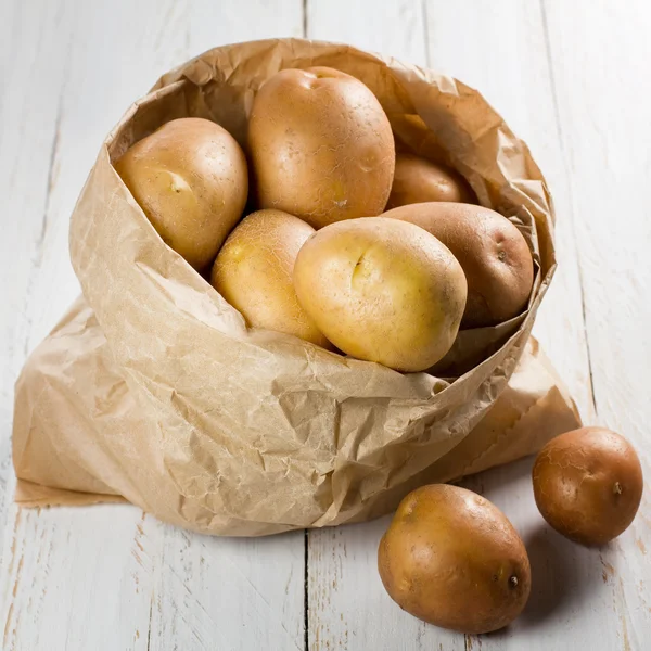 Potatoes in paper bag on vintage wooden table — Stock Photo, Image