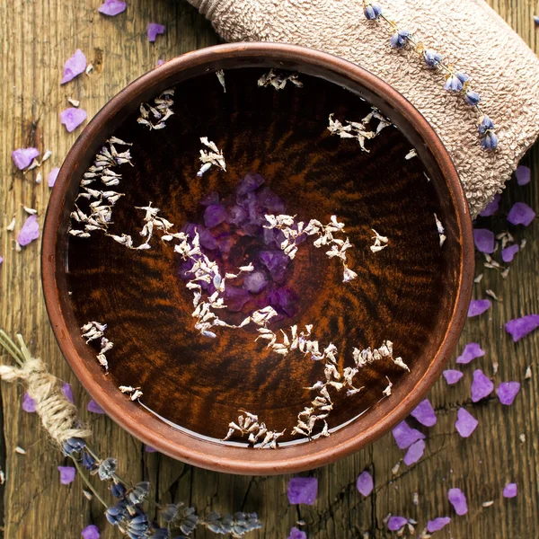 Cuenco de agua pura y pétalos de lavanda en la antigua superficie de madera. Composición de tratamientos Spa —  Fotos de Stock