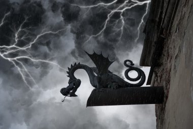 Frightening chimera on the facade of the old castle under thunderclouds and lightning clipart