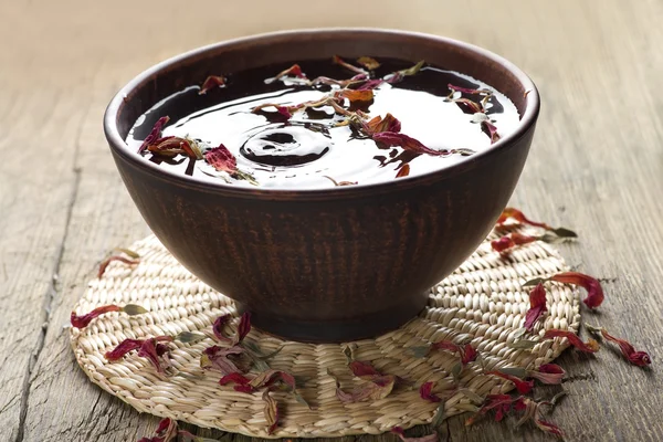 Tigela de água com pétalas de flores e em um tapete de palha em uma mesa de madeira vintage — Fotografia de Stock