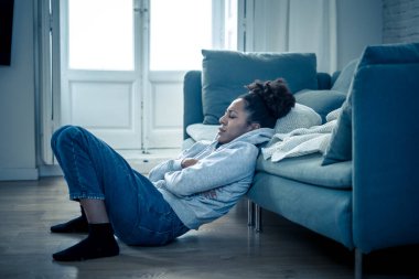 Üzgün ifadesi, baş ağrısı ve depresyonu olan depresif Afrikalı kadın kendini evinde çaresiz hissediyor. Afro-Amerikan gençliği ya da çekici siyah kadın düşünceli ve hasta bir şekilde kanepede acı ve endişe içinde yatıyor..