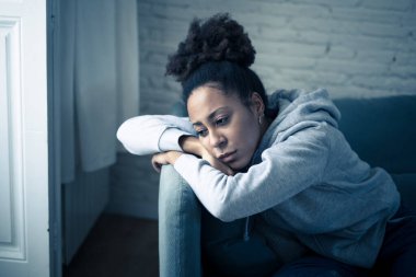 Üzgün ifadesi, baş ağrısı ve depresyonu olan depresif Afrikalı kadın kendini evinde çaresiz hissediyor. Afro-Amerikan gençliği ya da çekici siyah kadın düşünceli ve hasta bir şekilde kanepede acı ve endişe içinde yatıyor..