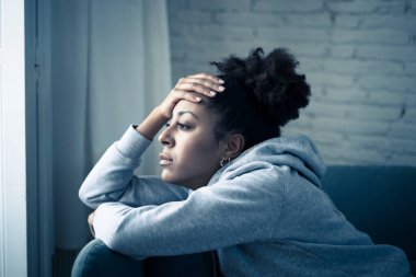 Üzgün ifadesi, baş ağrısı ve depresyonu olan depresif Afrikalı kadın kendini evinde çaresiz hissediyor. Afro-Amerikan gençliği ya da çekici siyah kadın düşünceli ve hasta bir şekilde kanepede acı ve endişe içinde yatıyor..