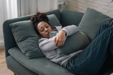 Genç ve çekici Afro-Amerikalı kadın oturma odasındaki kanepede uzanıyor üzgün ve endişeli hissediyor depresyon, sıkıntı ve endişe içinde zihinsel sağlık sorunları ve kırık kalp konsepti.