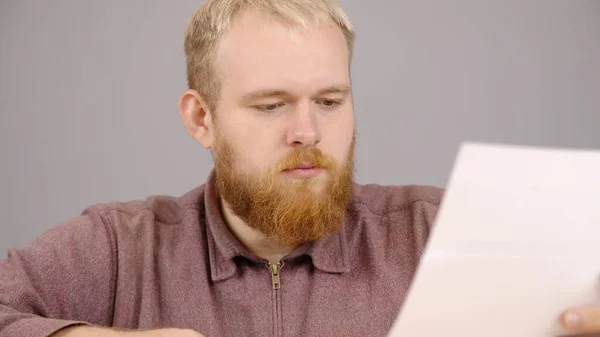 Cheerful male boss with beard sits at a table with documents in the office — 图库照片