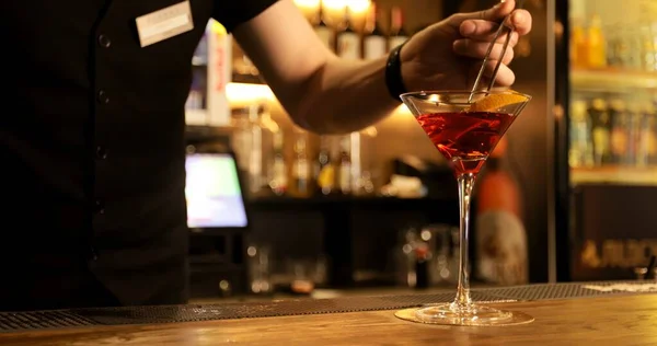 Barmen kırmızı kokteyli karıştırır ve güzel bir bardağa doldurur..