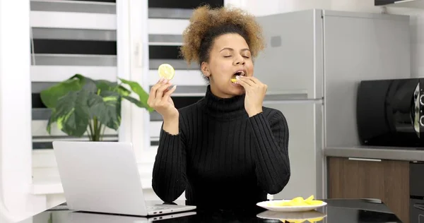 Молодая афро-американка ест лимон с тарелки на кухне.. — стоковое фото