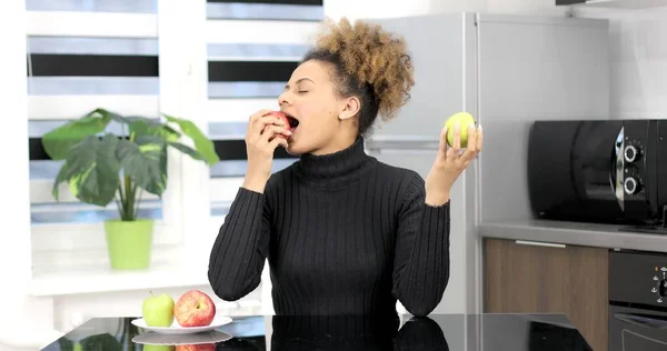 Musta nainen istuu keittiössä ja syö hedelmiä.. tekijänoikeusvapaita valokuvia kuvapankista