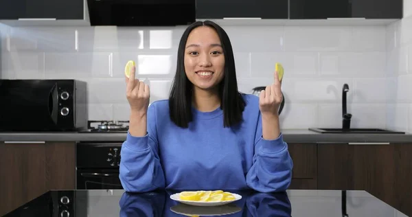 Jovem menina asiática comendo limão de um prato na cozinha. — Fotografia de Stock