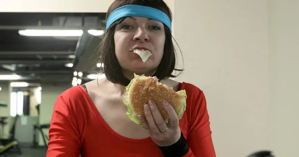 Aç şişman kadın spor salonunda büyük bir hamburger yiyor.. 