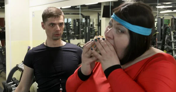 배고픈 뚱뚱 한 여자 가 체육관에서 큰 햄버거를 먹고 있어요. — 스톡 사진