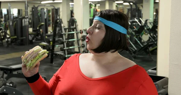 Aç şişman kadın spor salonunda büyük bir hamburger yiyor.. 