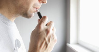 Pencerenin yanında elektronik sigarası olan yakın plan bir adam.. 