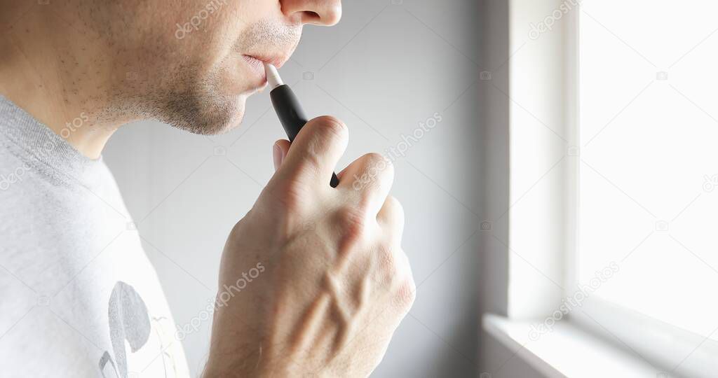 Close-up man with electronic cigarette near the window. 