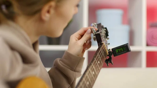 Yakın plan kız elleri gitar akort ediyor. Akustik gitar mandallarını kontrol eden genç bir kadın..
