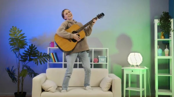 Neşeli kız gitar çalıyor ve kanepede dans ediyor..