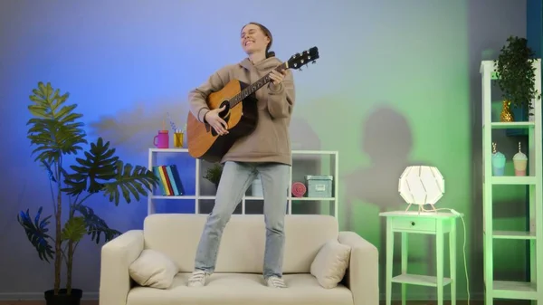 Neşeli kız gitar çalıyor ve kanepede dans ediyor..