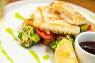 Sebzeli, patatesli ve limonlu kalamar. Bir bardak şarapla servis edilir.