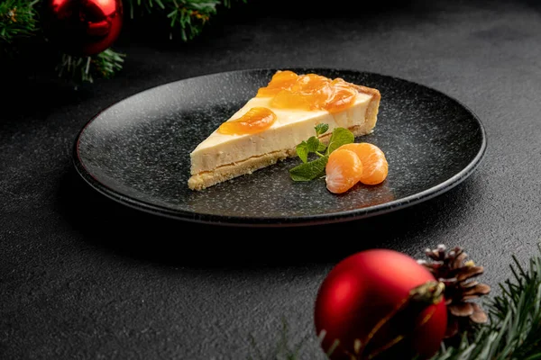 Siyah bir tabakta servis edilen mandalina ve nane şekeriyle süslenmiş mandalina tatlısı. Kara Noel arkaplanı üzerine yemek