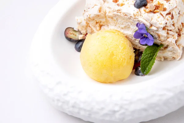 meringue dessert with a scoop of ice cream, decorated with violet and mint leaf