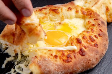 Bir parça khachapuri 'yi koyu bir arka planda yumurtaya batırır.