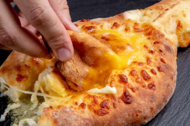 Bir parça khachapuri 'yi koyu bir arka planda yumurtaya batırır.