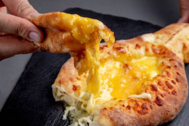 Bir parça khachapuri 'yi koyu bir arka planda yumurtaya batırır.