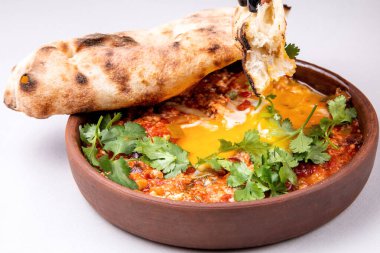 Şifalı bitkilerle, peynirle ve arka planda taze hamur işleriyle Shakuka.