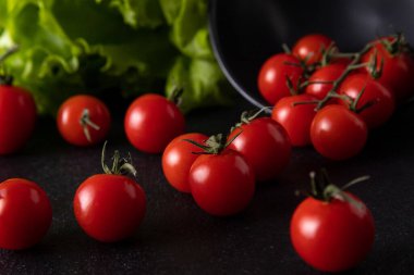 cherry tomatoes dropped from the plate. dark background decorated with salad leaves