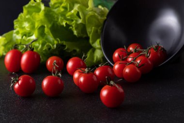 cherry tomatoes dropped from the plate. dark background decorated with salad leaves