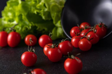 cherry tomatoes dropped from the plate. dark background decorated with salad leaves