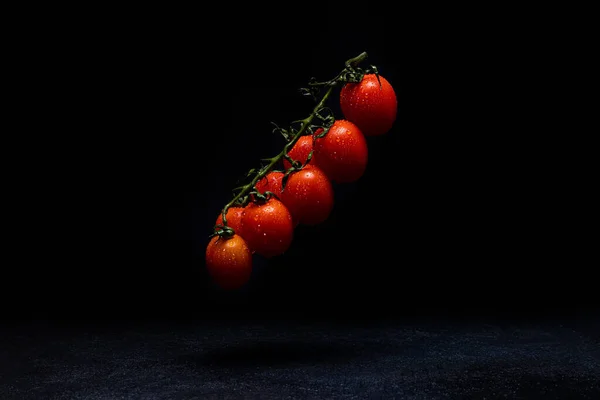 cherry tomatoes on a vect on a dark background hanging above the surface tomatoes in drops of water