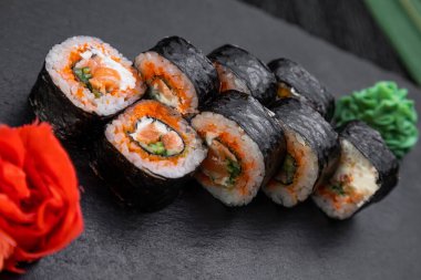 Suşi ruloları bambu yaprakları ve çubuklarla süslenmiş karanlık bir arka planda serili.