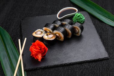 Suşi ruloları bambu yaprakları ve çubuklarla süslenmiş karanlık bir arka planda serili.