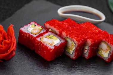 Suşi ruloları bambu yaprakları ve çubuklarla süslenmiş karanlık bir arka planda serili.