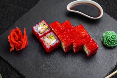 Suşi ruloları bambu yaprakları ve çubuklarla süslenmiş karanlık bir arka planda serili.