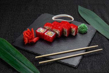 Suşi ruloları bambu yaprakları ve çubuklarla süslenmiş karanlık bir arka planda serili.