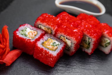 Suşi ruloları bambu yaprakları ve çubuklarla süslenmiş karanlık bir arka planda serili.