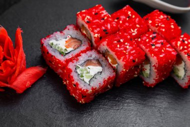 Suşi ruloları bambu yaprakları ve çubuklarla süslenmiş karanlık bir arka planda serili.