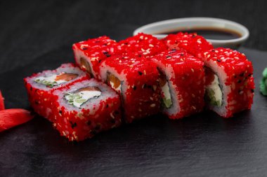 Suşi ruloları bambu yaprakları ve çubuklarla süslenmiş karanlık bir arka planda serili.