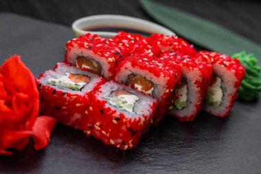 Suşi ruloları bambu yaprakları ve çubuklarla süslenmiş karanlık bir arka planda serili.