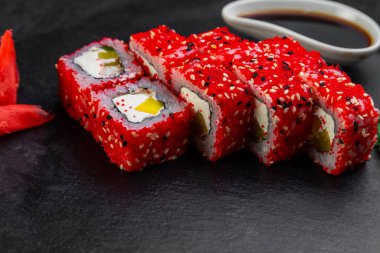 Suşi ruloları bambu yaprakları ve çubuklarla süslenmiş karanlık bir arka planda serili.