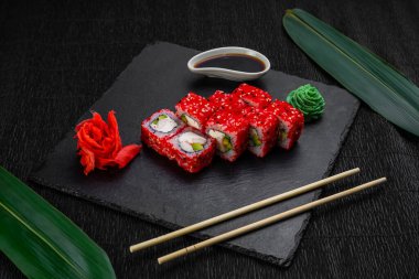 Suşi ruloları bambu yaprakları ve çubuklarla süslenmiş karanlık bir arka planda serili.