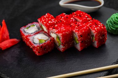 Suşi ruloları bambu yaprakları ve çubuklarla süslenmiş karanlık bir arka planda serili.