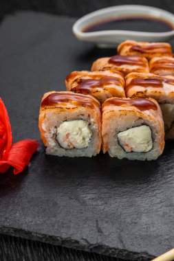 Suşi ruloları bambu yaprakları ve çubuklarla süslenmiş karanlık bir arka planda serili.