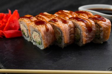 Suşi ruloları bambu yaprakları ve çubuklarla süslenmiş karanlık bir arka planda serili.