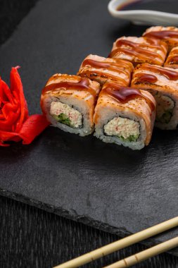 Suşi ruloları bambu yaprakları ve çubuklarla süslenmiş karanlık bir arka planda serili.