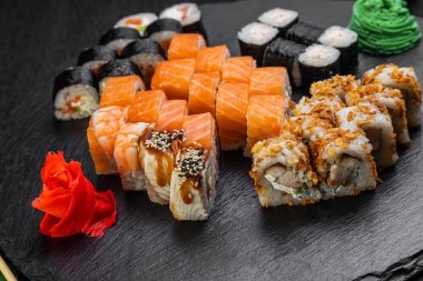 Suşi ruloları bambu yaprakları ve çubuklarla süslenmiş karanlık bir arka planda serili.