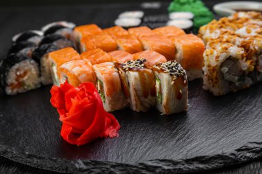 Suşi ruloları bambu yaprakları ve çubuklarla süslenmiş karanlık bir arka planda serili.